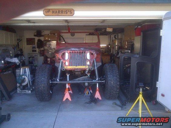 Jeep CJ on jack stands in garage, front end disassembled. Doors off