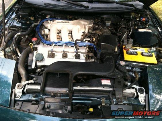 Engine bay of a green car, showing the V6 engine, battery, and radiator