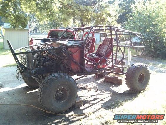 Custom buggy with roll cage, red seats, and large tires. Red pickup truck in background