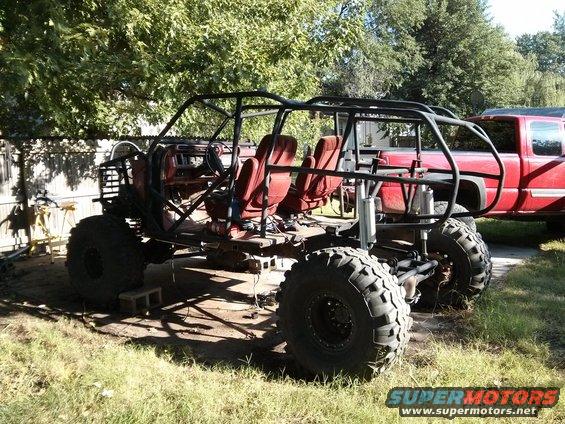 Custom off-road buggy with red seats and roll cage, parked outdoors next to a red pickup truck
