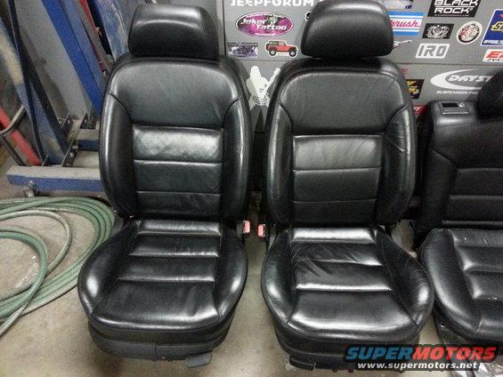 Two black leather car seats with adjustable headrests and visible seatbelt buckles