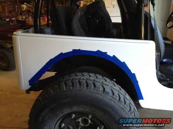 White Jeep fender with blue tape marking cut lines for tire clearance
