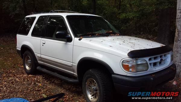 white Ford Explorer parked in woods, leaves on hood