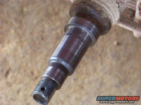 Close-up of a metal automotive spindle with threaded end and a small hole