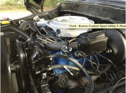 Engine bay of a Ford Bronco, showing the V8 engine and air cleaner assembly. Text overlay says 'Ford - Bronco Custom Sport Utility 2-Door'