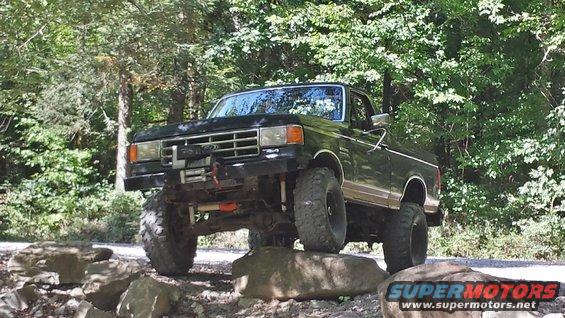 Black 1987 Ford Bronco with lifted suspension and large tires driving over rocks