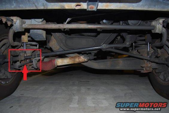 Undercarriage of a vehicle showing suspension and steering components, with a red arrow pointing to a part