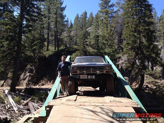 1986 Ford Bronco on a wooden bridge with a man standing beside it