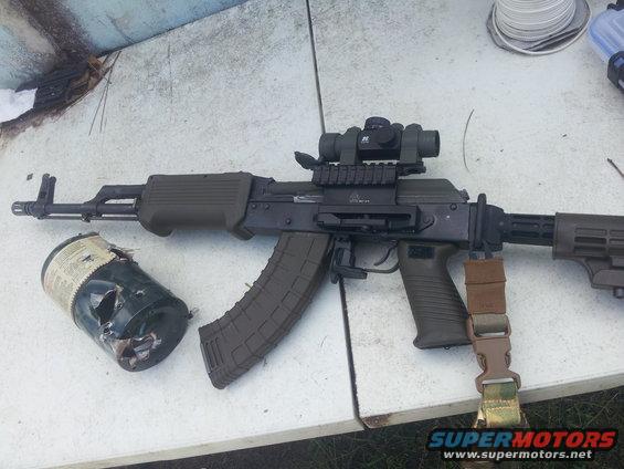 Assault rifle with scope and a damaged canister on a table
