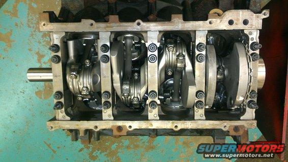 Engine block with crankshaft and connecting rods visible, showing internal components. Watermark reads SUPERMOTORS