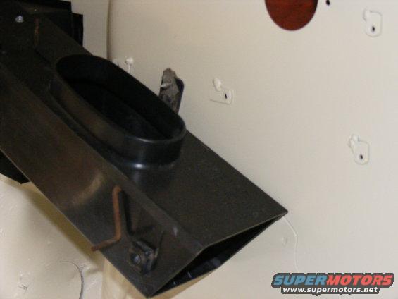 Black air duct with oval opening, attached to a cream-colored surface