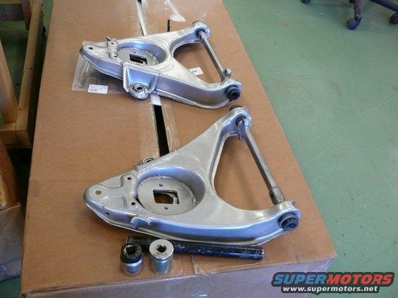 Two aluminum suspension control arms and hardware on a cardboard box