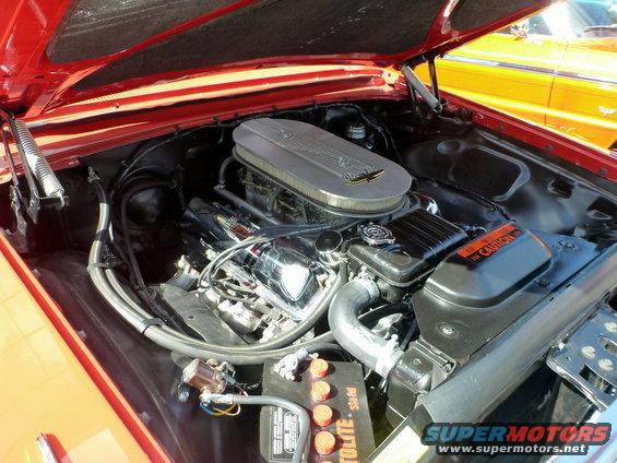Red engine bay with chrome details and a large air filter housing. A yellow car is visible in the background