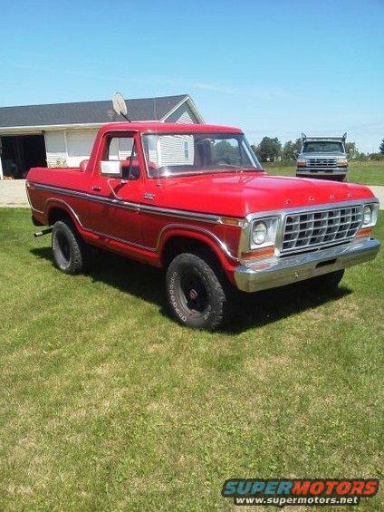 Red 1978 Ford Bronco parked on grass with a second truck in the background