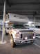 2008 Ford F-450 - A Ford truck with a camper shell is parked under a covered structure next to a boat.