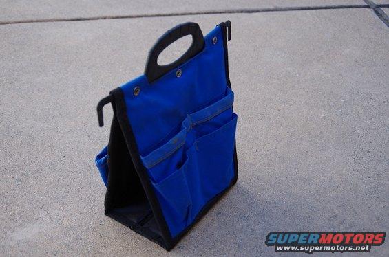 Blue fabric tool bag with black handle and pockets, resting on concrete