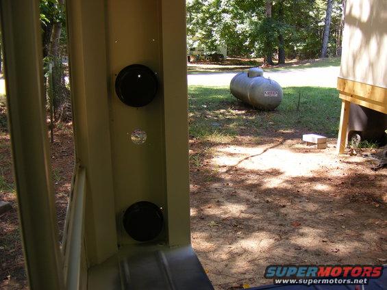 Interior view of a tan vehicle showing two black speakers and a glimpse of the outdoors with a large propane tank