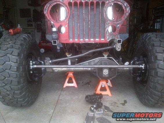 1985 Jeep CJ7 front axle and suspension on jack stands, undergoing modification. Large tires are mounted