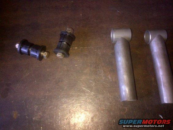 two black suspension bushings with bolts and two metal tubes on a surface