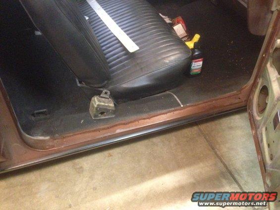 Car interior showing the passenger side floor, seat, and door jamb. A bottle of cleaner is on the seat