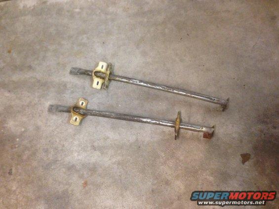 Two metal rods with mounting brackets on a concrete floor