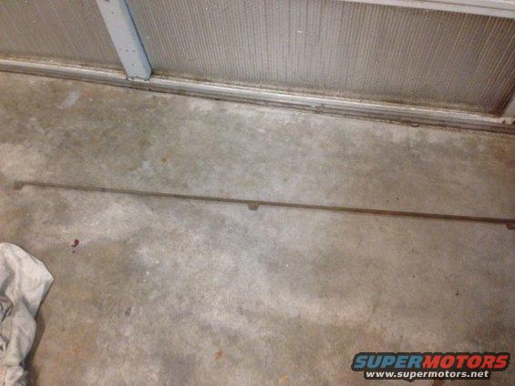 Long, thin metal trim piece with two small brackets, lying on a concrete floor