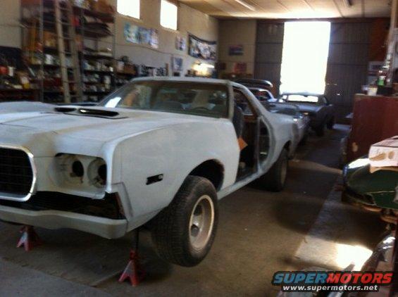 Unpainted car on jack stands, front end disassembled, hood scoop, open door