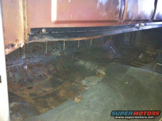 Interior of a rusty vehicle showing floor and lower door panel