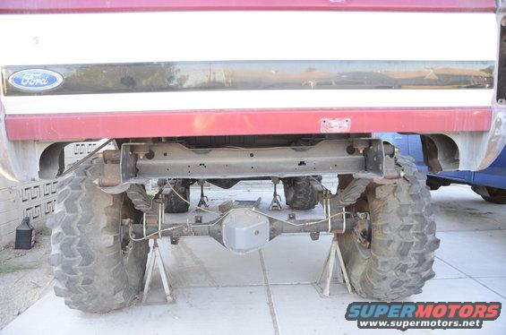 Rear axle and suspension components of a Ford truck, lifted on jack stands. Another vehicle is partially visible to the right