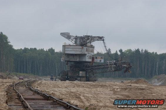 Bucket-wheel excavator in a sandy quarry with train tracks in the foreground and a forest in the background