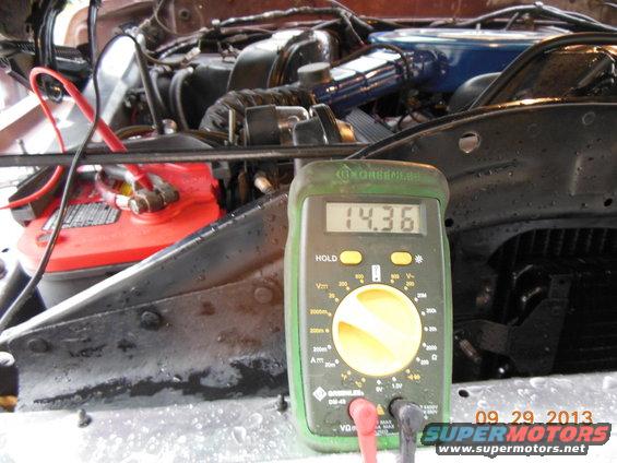 1979 Ford F-150 engine bay with multimeter reading 14.36V next to red battery