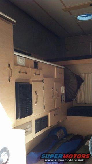Camper interior with light wood cabinets, black vents, and sleeping bags