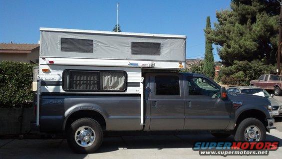 Gray Ford F-250 Super Duty crew cab truck with a pop-up camper shell, parked outside. Another truck is visible in the background