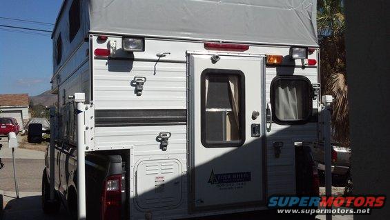 Rear view of a truck with a camper shell mounted in the bed. Camper has a door and windows