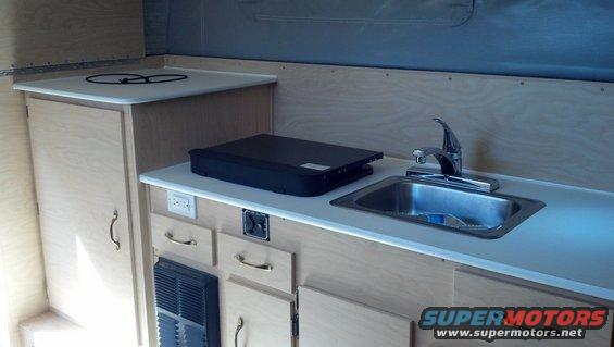 Camper interior with sink, faucet, portable stove, and cabinets
