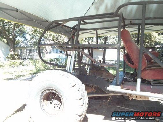 Custom off-road vehicle frame with red seats and large tire, side view