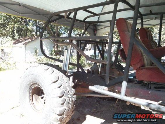 Custom buggy frame with red seats and large off-road tire, parked under a canopy