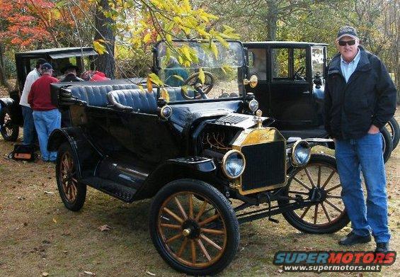 Man standing next to a black 1915 Ford Model T touring car. Another Model T is behind it