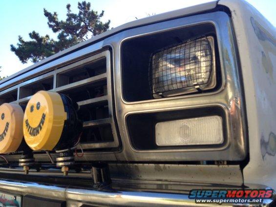 Close-up of a Ford truck grille with two yellow smiley face lights and a headlight with a wire mesh cover