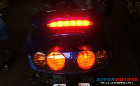 Rear view of a blue scooter with illuminated tail lights and brake light