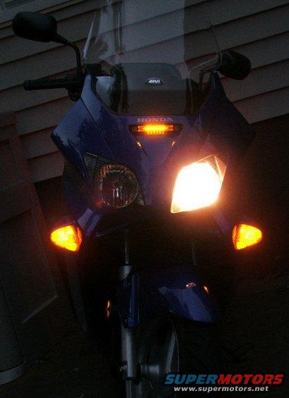 Front view of a blue scooter with its headlights and turn signals on. The HONDA logo is visible