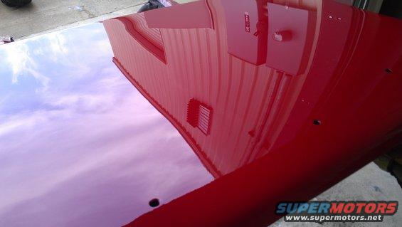 Red car hood with reflection of a building and sky. Two holes visible on the hood