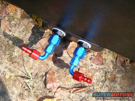 two blue and red fuel line fittings attached to a dark surface, lying on the ground with leaves