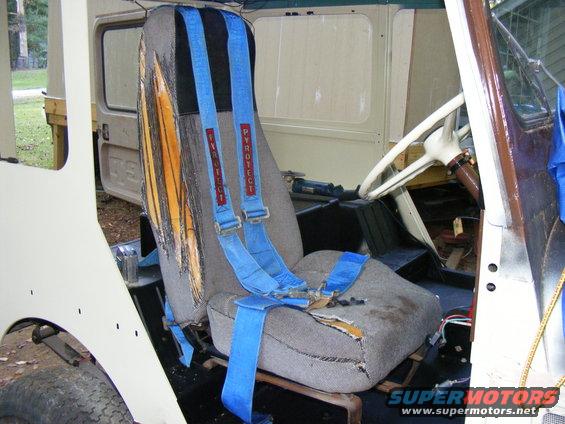 Interior view of a vehicle with torn seats and blue racing harnesses with "PYROTECT" text