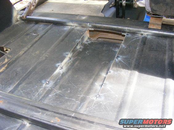 Vehicle floor pan showing welded metal patches and roll bar supports