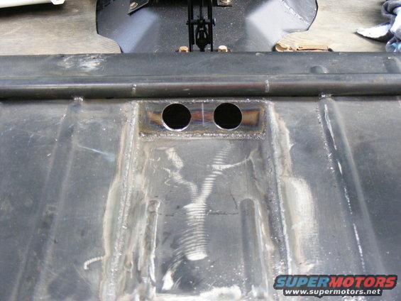 Underbody of a vehicle showing two circular holes and metal bracing