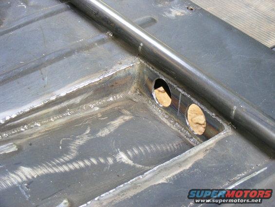 Close-up of metal frame with two circular cutouts and a welded bar. Some weld marks and scratches visible
