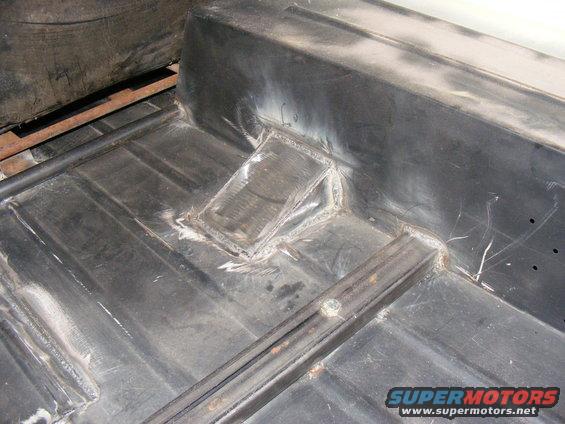Close-up of a vehicle's metal floor pan with visible welds and repair work