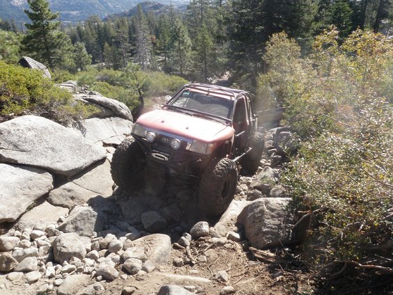 Red off-road vehicle with large tires navigating a rocky trail