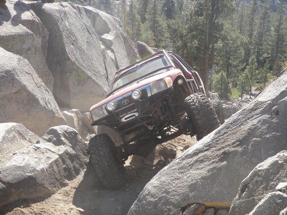 Modified Toyota SUV with roll cage navigating a rocky trail. Winch visible on front bumper